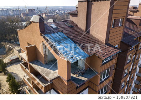 Aerial top view of unfinished tall apartment building, annex room under construction, high chimneys and plastic windows on tiled roof. 139807921