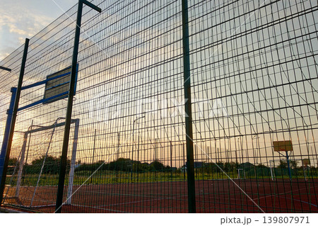 Outdoors mini football and basketball court with ball gate and basket surrounded with high protective fence. Outdoors mini football and basketball court with ball gate and basket surrounded with high protective fence. 139807971