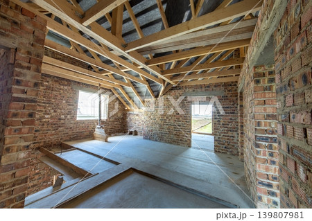 Attic of a building under construction with wooden beams of a roof structure and brick walls. Attic of a building under construction with wooden beams of a roof structure and brick walls. 139807981