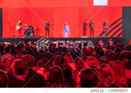 Live concert crowd watching band on stage with red lighting and singer 139808003