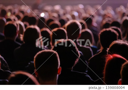 Audience in dimly lit venue watching performance, crowd silhouettes at indoor event 139808004