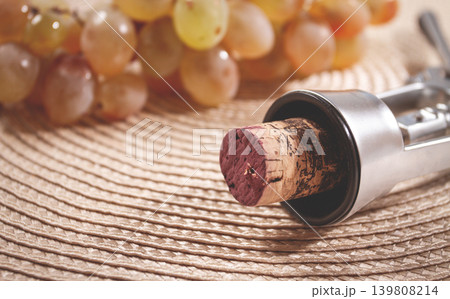 A corkscrew with a wine bottle stopper, lying on a woven napkin, with green grapes, A corkscrew with a wine bottle stopper, lying on a woven napkin, with green grapes, 139808214