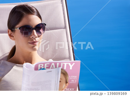 Woman, reading and magazine on sunbed outdoor with sunglasses for relax, article or lifestyle news. Person, publication and paper by pool on holiday, vacation and summer trip at hotel or mockup space Woman, reading and magazine on sunbed outdoor with sunglasses for relax, article or lifestyle news. Person, publication and paper by pool on holiday, vacation and summer trip at hotel or mockup space 139809169