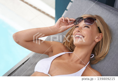 Woman, bikini and relax at pool in summer with sunglasses for holiday swimming, outdoor or vacation. Female person, sun bathing and smile on patio furniture with shades for rest, wellness or Miami Woman, bikini and relax at pool in summer with sunglasses for holiday swimming, outdoor or vacation. Female person, sun bathing and smile on patio furniture with shades for rest, wellness or Miami 139809215