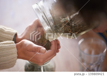 Hands, jar and tea leaves for herbal drink in kitchen for healthy benefits for beverage or hibiscus, jasmine or preparation. Person, fingers and chamomile for peaceful morning, vitality or wellness 139809421