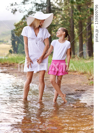 Mother, daughter and happiness outdoor in lake for bonding, support or holding hands on holiday in nature. Family, woman and girl child with smile or adventure on vacation, travel and river with love 139809796