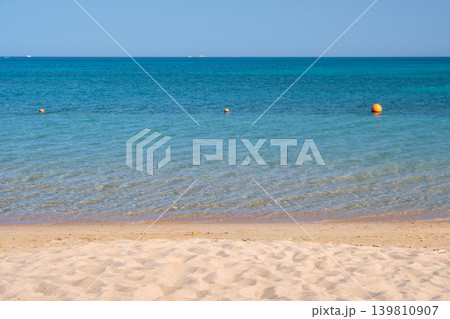 Seascape with surface of blue sea water with small ripple waves crashing on yellow sandy beach. Travel and vacations concept. Seascape with surface of blue sea water with small ripple waves crashing on yellow sandy beach. Travel and vacations concept. 139810907