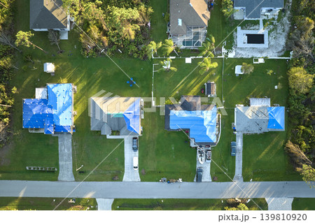 Aerial view of damaged in hurricane Ian houses roofs covered with blue protective tarp against rain water leaking until replacement of asphalt shingles Aerial view of damaged in hurricane Ian houses roofs covered with blue protective tarp against rain water leaking until replacement of asphalt shingles 139810920