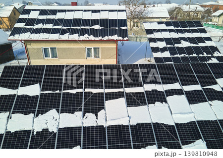 Aerial view of house roof with solar panels covered with snow melting down in winter end for producing clean energy. Concept of low effectivity of renewable electricity in northern region Aerial view of house roof with solar panels covered with snow melting down in winter end for producing clean energy. Concept of low effectivity of renewable electricity in northern region 139810948