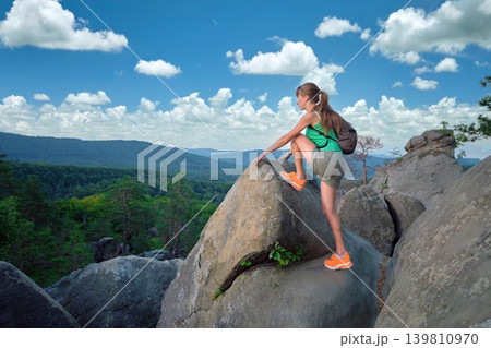 Sportive woman climbing alone on hillside rocky trail. Female hiker overcoming difficult cliff on wilderness path. Active lifestyle concept Sportive woman climbing alone on hillside rocky trail. Female hiker overcoming difficult cliff on wilderness path. Active lifestyle concept 139810970