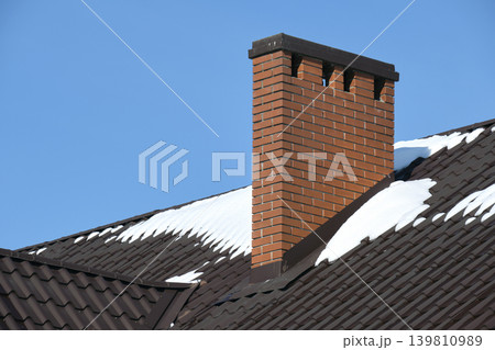 Closeup of house roof top covered with snow in cold winter. Tiled covering of building in wintertime weather Closeup of house roof top covered with snow in cold winter. Tiled covering of building in wintertime weather 139810989