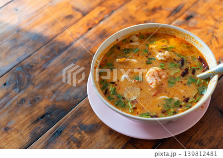 Traditional Thai tom yum goong shrimp herbs spicy sour broth served hot in bowl on wooden table Traditional Thai tom yum goong shrimp herbs spicy sour broth served hot in bowl on wooden table 139812481