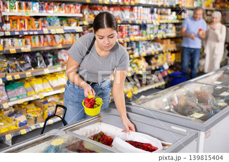 Young girl choosing frozen peppers in freezer in grocery store Young girl choosing frozen peppers in freezer in grocery store 139815404