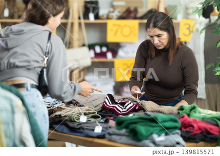 Two selective women choosing pantaloons and pullovers in clothing store Two selective women choosing pantaloons and pullovers in clothing store 139815571