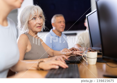 Portrait of an elderly positive woman working on computer with group of friends while attending PC classes in nursing home Portrait of an elderly positive woman working on computer with group of friends while attending PC classes in nursing home 139815675