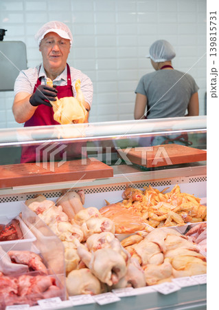 Adult man seller lays out chicken in butcher shop Adult man seller lays out chicken in butcher shop 139815731