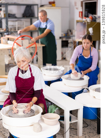 Mature woman learning how to create pottery on potter wheel in workshop 139815828