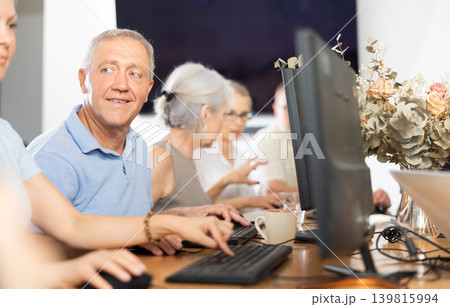 Positive elderly man using computer to surf internet in library Positive elderly man using computer to surf internet in library 139815994