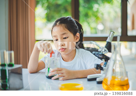 little scientist looking through a microscope and test tubes filled with chemicals for learning about science and experiments. 139816088