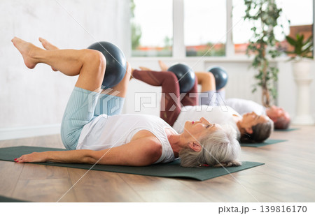 People lying on karemat, pulled bent legs to themselves and clamped soft-ball in knee 139816170