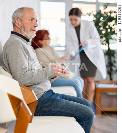 Elderly people wait in line at clinic. Nurse talks to patient in background 139816265