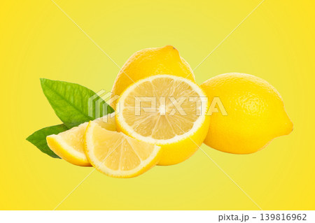 Two whole lemons with a sliced lemon and green leaves nearby 139816962