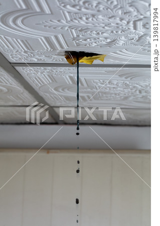 Water leaking through damaged ceiling tile inside house during rainstorm. Ceiling water leak from broken roof or pipe inside residential home 139817994