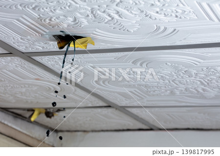Water leaking through damaged ceiling tile inside house during rainstorm. Ceiling water leak from broken roof or pipe inside residential home 139817995