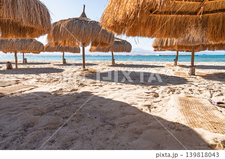 Straw beach umbrellas casting shade over a sandy shoreline at a Red Sea resort near Dahab, Eg 139818043