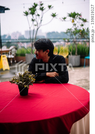 Asian man daydreaming while sitting at outdoor reception table Asian man daydreaming while sitting at outdoor reception table 139819127