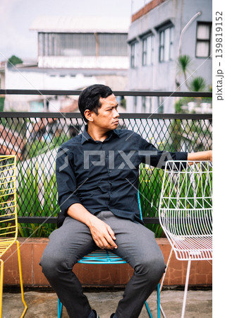 Thoughtful young man relaxing on vibrant outdoor patio chair Thoughtful young man relaxing on vibrant outdoor patio chair 139819152