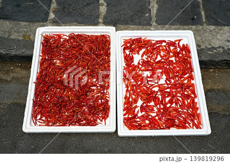 Bright red dried chili peppers spread out in white styrofoam trays on street pavement for sun drying at outdoor market in Hoi An Vietnam Bright red dried chili peppers spread out in white styrofoam trays on street pavement for sun drying at outdoor market in Hoi An Vietnam 139819296