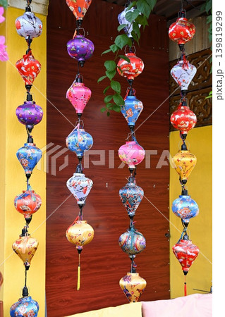 Colorful traditional Hoi An silk lanterns with floral patterns hanging in rows against yellow wall at outdoor souvenir market in Vietnam 139819299