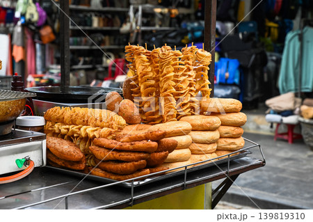 A metal tray stacked with various golden snacks like tornado potatoes and donuts at a street food market stall in Hoi An Vietnam A metal tray stacked with various golden snacks like tornado potatoes and donuts at a street food market stall in Hoi An Vietnam 139819310