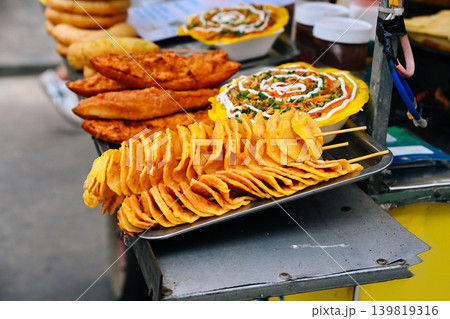 Crispy golden tornado potatoes on skewers are served on a metal tray at a traditional street food market stall in Hoi An Vietnam Crispy golden tornado potatoes on skewers are served on a metal tray at a traditional street food market stall in Hoi An Vietnam 139819316