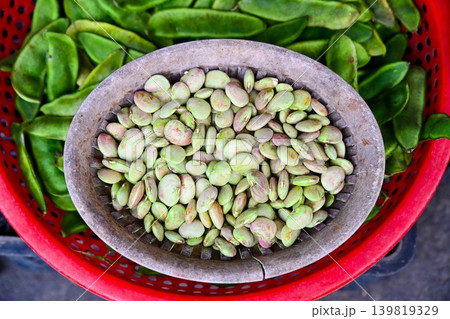 A close up top view of fresh raw lima beans in a wicker basket with green pods in a red plastic tray at a street market stall in Vietnam 139819329