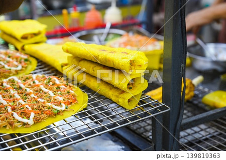 Traditional crisp yellow savory pancakes and vietnamese rice paper pizza displayed on metal wire rack at outdoor street food market stall in Vietnam 139819363