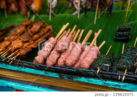 Traditional grilled pork meatballs nem nuong and meat wrapped in betel leaves bo la lot on skewers at outdoor street food market in Vietnam 139819375