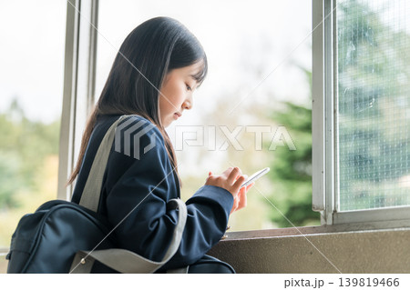 校舎の廊下でスマホを使う小学生,中学生,高校生の女の子（落ち込む,寂しい,ひとりぼっち） 139819466