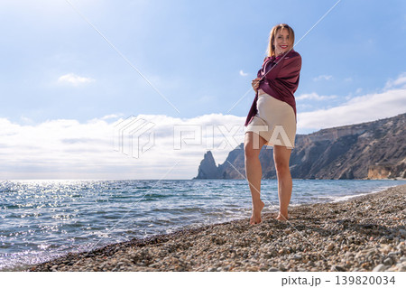 Woman beach ocean happy mature woman posing on a pebble shore with cliffs in the background and copy space Woman beach ocean happy mature woman posing on a pebble shore with cliffs in the background and copy space 139820034