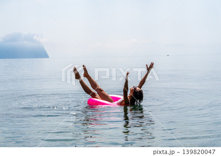 Woman inflatable sea floating on a pink ring with raised legs and arms during a joyful summer vacation at the beach Woman inflatable sea floating on a pink ring with raised legs and arms during a joyful summer vacation at the beach 139820047