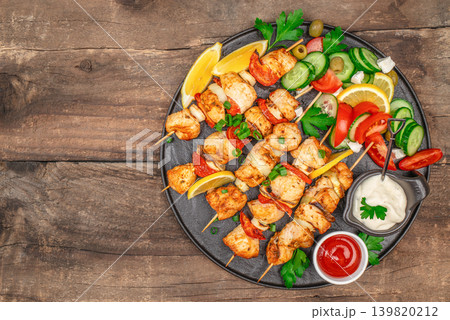 Chicken skewers with fresh salad and sauces on wooden table Chicken skewers with fresh salad and sauces on wooden table 139820212