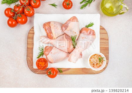 Raw chicken drumsticks with tomatoes and rosemary on cutting board top view Raw chicken drumsticks with tomatoes and rosemary on cutting board top view 139820214