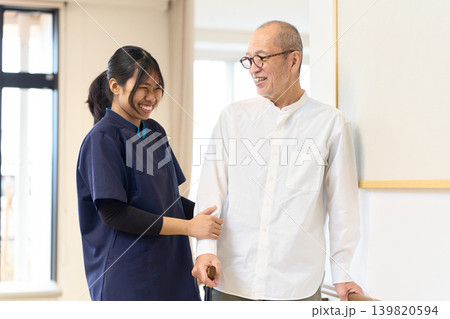 手すりと杖を使って歩く練習をするシニアと外国人介護士 手すりと杖を使って歩く練習をするシニアと外国人介護士 139820594