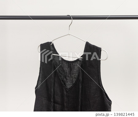 Black women sleeveless blouse hanging on hanger. Lightweight garment suspended from clothing rail. Female summer wardrobe clothing for casual outfit. Black women sleeveless blouse hanging on hanger. Lightweight garment suspended from clothing rail. Female summer wardrobe clothing for casual outfit. 139821445