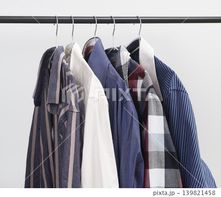 Group of shirts hanging on metal rack. Clothing garments arranged on hangers. Male wardrobe shirt assortment concept.. 139821458