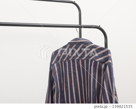 Striped shirt placed on curved rack. Apparel draped over metal hanger. Fashion storage wardrobe planning concept.. Striped shirt placed on curved rack. Apparel draped over metal hanger. Fashion storage wardrobe planning concept.. 139821535