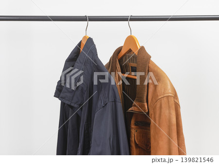 Two jackets hanging on clothing rack. Garments suspended from wooden hangers. Menswear outerwear selection for seasonal wardrobe.. 139821546