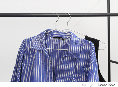 Wrinkled striped women blouse hanging on hanger. Garment suspended from clothing rail. Female wardrobe shirt with crumpled unironed fabric texture. Wrinkled striped women blouse hanging on hanger. Garment suspended from clothing rail. Female wardrobe shirt with crumpled unironed fabric texture. 139821552