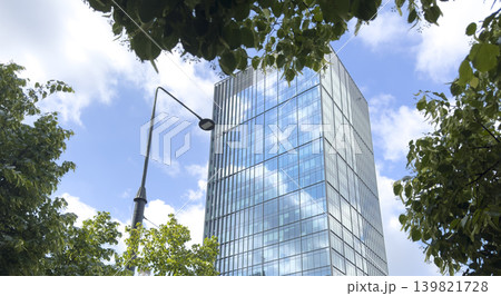 Modern glass skyscraper with green foliage elements against city sky. Contemporary urban 139821728